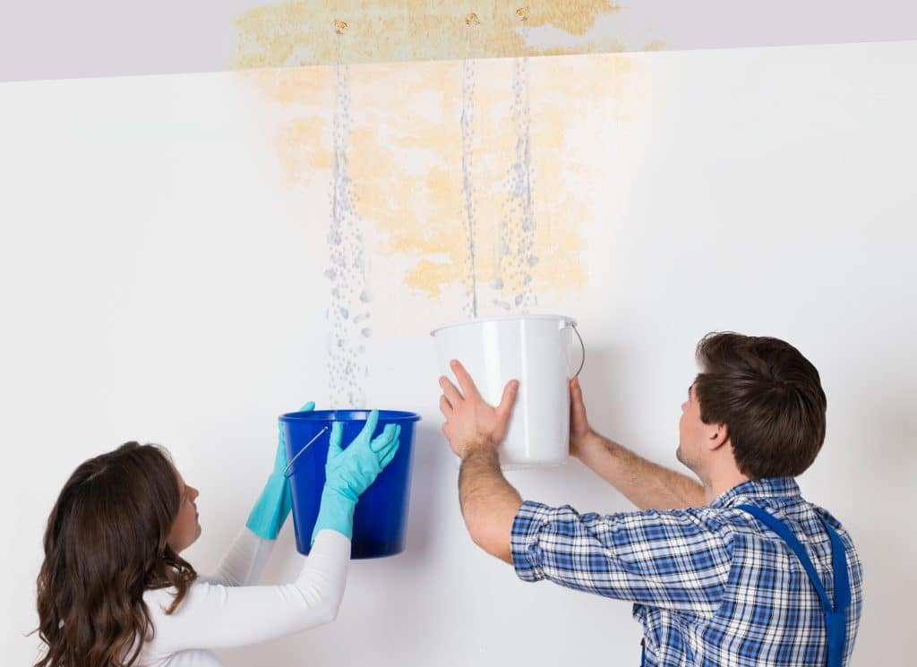 A couple holds buckets under water leaking from their ceiling.