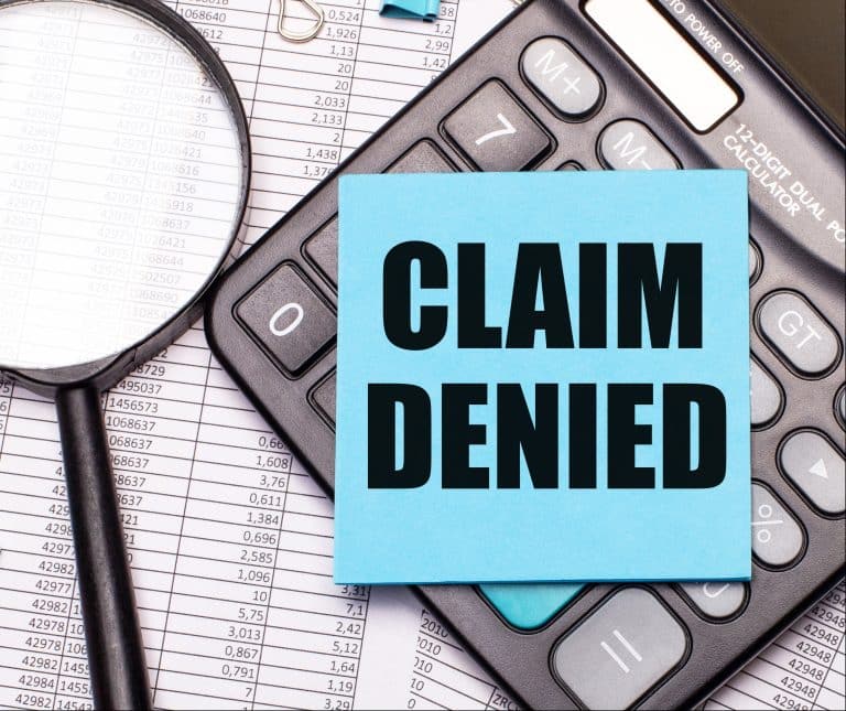A note saying “claim denied” over a stack of insurance papers.