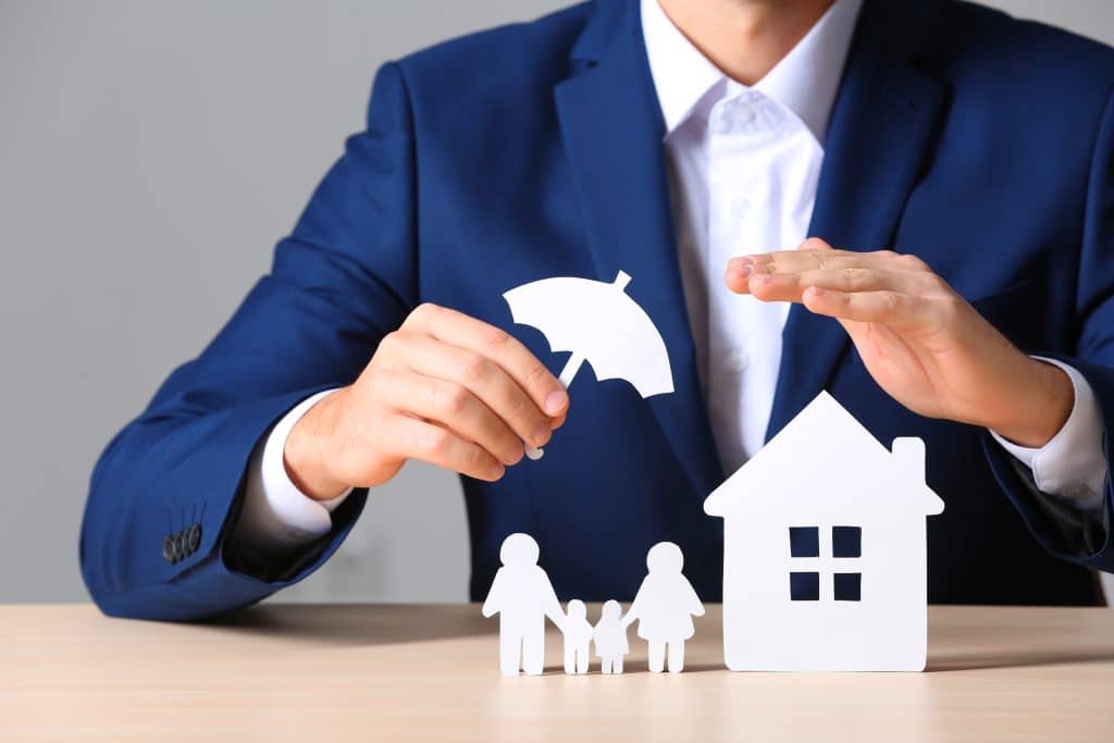 Insurance agent holding umbrella over paper family and home signifying umbrella insurance.