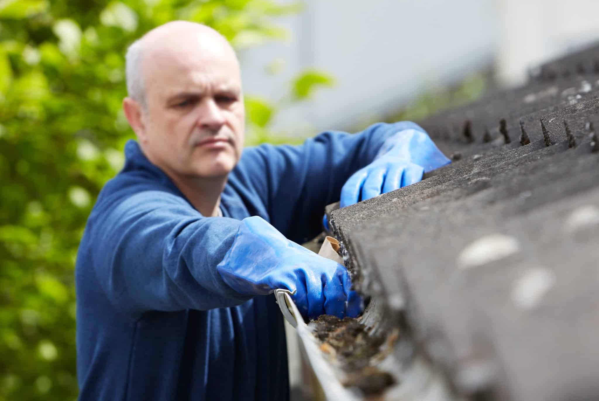 Man cleaning leaves out of his gutters.