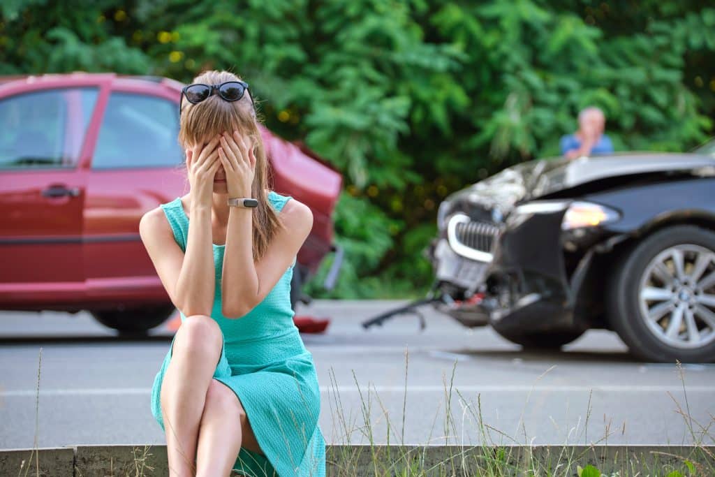 Woman covering her face on the side of the road after a car accident