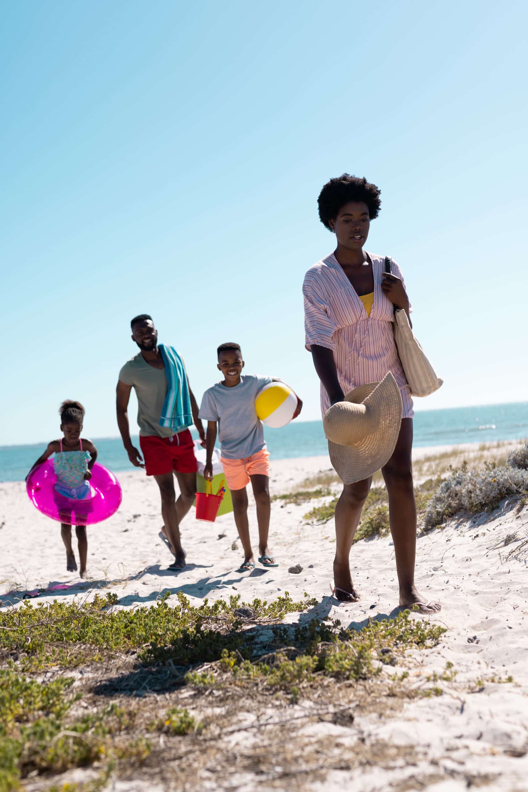 African american parents and children walking on sandy beach against clear blue sky during vacation. Copy space, unaltered, family, together, childhood, picnic, nature, vacation, enjoyment, summer.